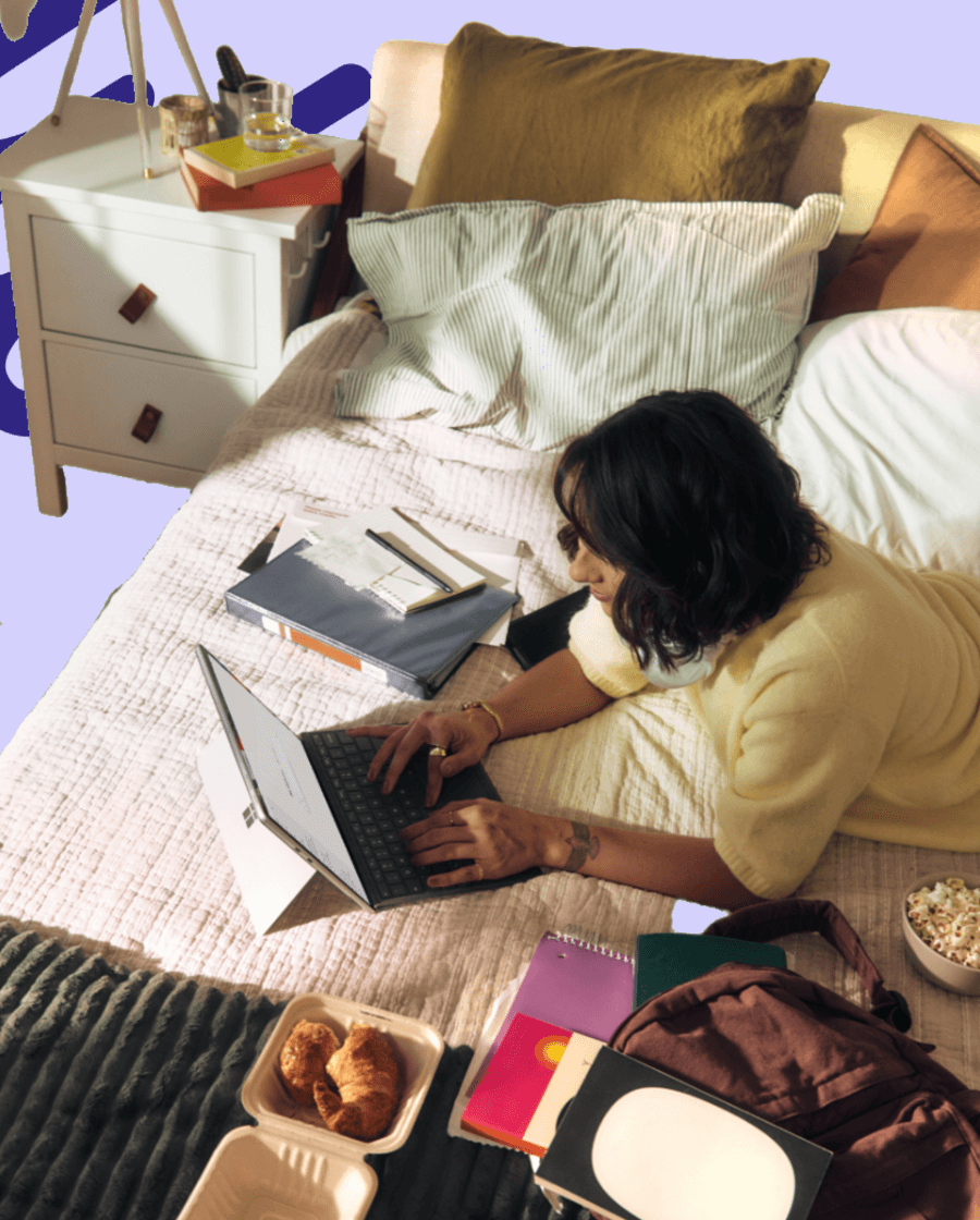 Frau arbeitet mit dem Laptop auf dem Bett, um sie herum Unterlagen und Notizbücher